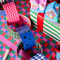 Styled holiday scene showing the paper chains partly assembled into a garland with plaid, checkered, and ornament patterns among wrapped gifts and a gingerbread house.