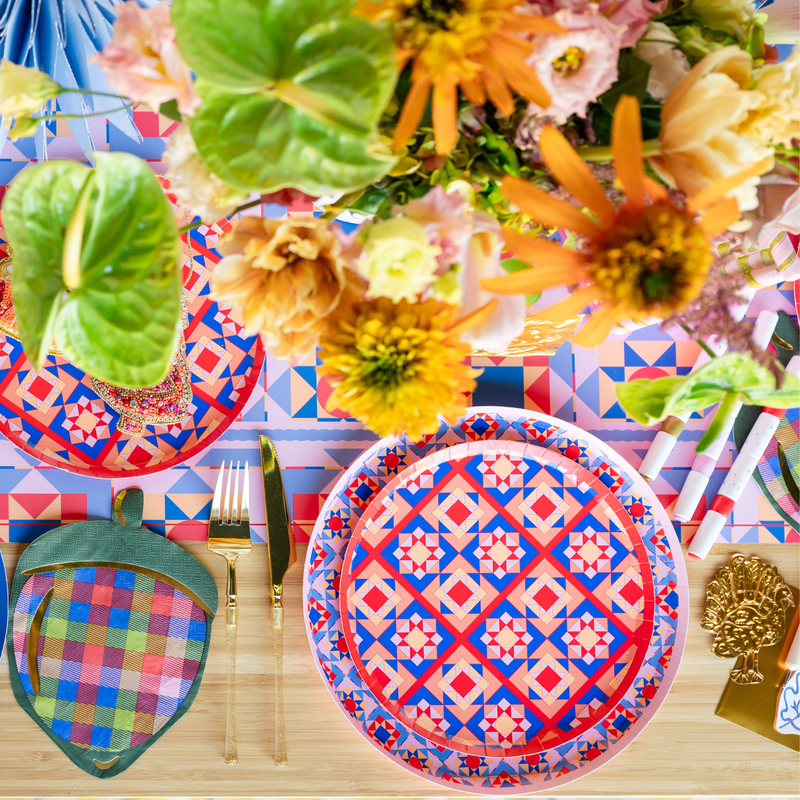 Overhead holiday place setting showing the quilt-pattern plate with a plaid strawberry napkin, a green plate, and vibrant autumn décor with florals.