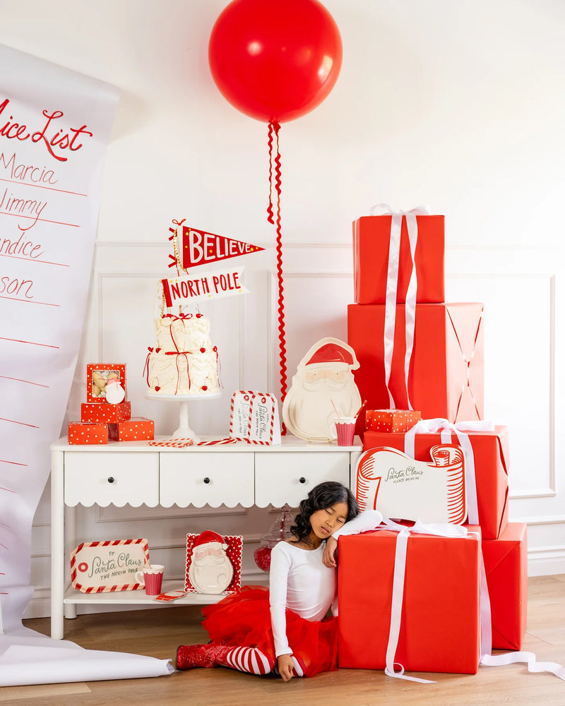 Complete Christmas Party Kit tableware set displayed on a counter with cake, gifts, and Merry Christmas banner, showcasing the red and white party supplies for holiday decor.