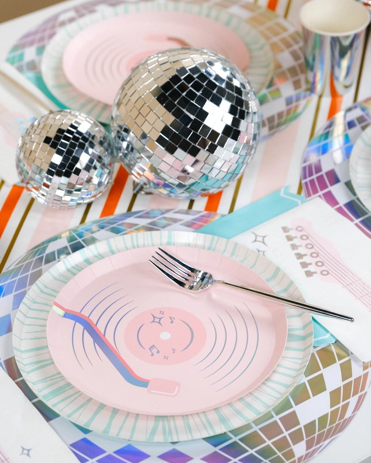 Close-up of a pink record-themed plate nested on top of a holographic disco ball charger for a professional party look.