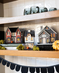 Three glitter Halloween village houses styled on a kitchen shelf with books, moss and a white pumpkin