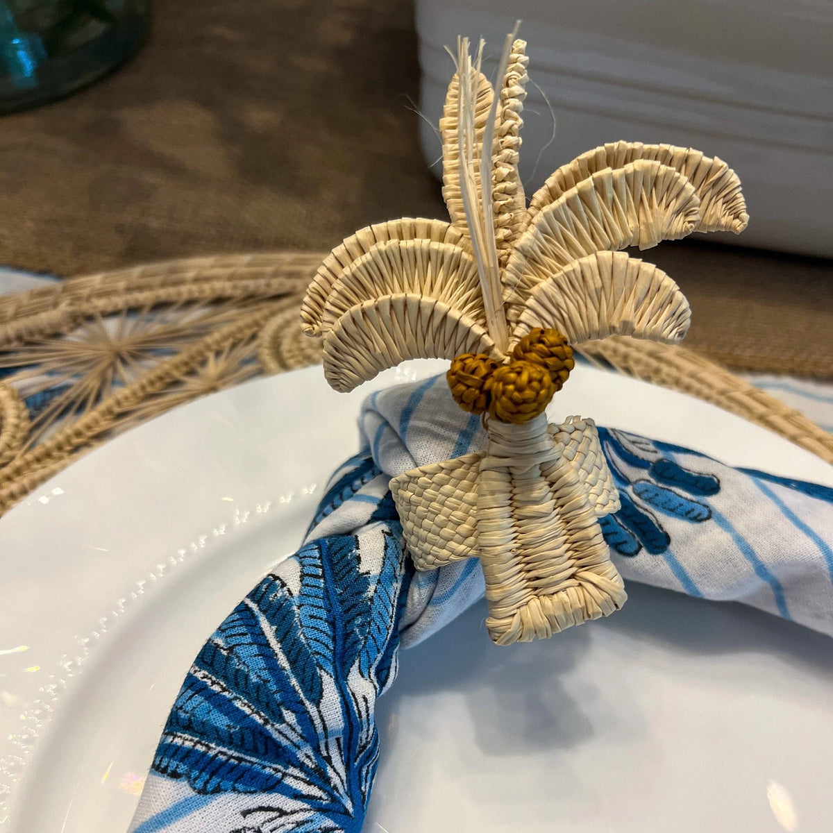 Escape to the tropics at every meal with our woven Palm Tree Napkin Rings. Crafted to complement your tropical table decor, these napkin rings feature natural-colored palm trees with brown coconuts, adding a coastal touch to your table. Perfect for hosting a luau or simply spicing up dinner, these palm tree napkin rings offer an instant vacation vibe.
