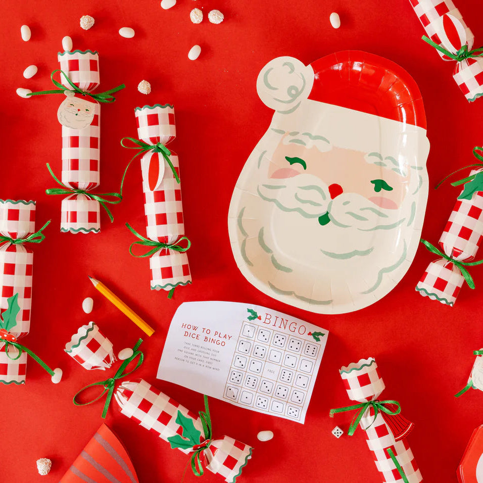 Christmas poppers scattered around an interactive holiday game card and a Santa-shaped plate on a red background.
