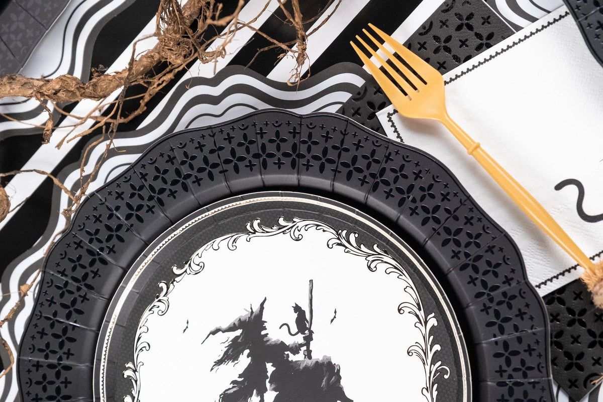 Close up detail showing the intricate die-cut edge of the black paper dinner plate next to gold flatware.
