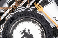 Close up detail showing the intricate die-cut edge of the black paper dinner plate next to gold flatware.