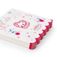 Angled stack of white large party napkins with illustrated birthday icons and hot pink scalloped edge on white background