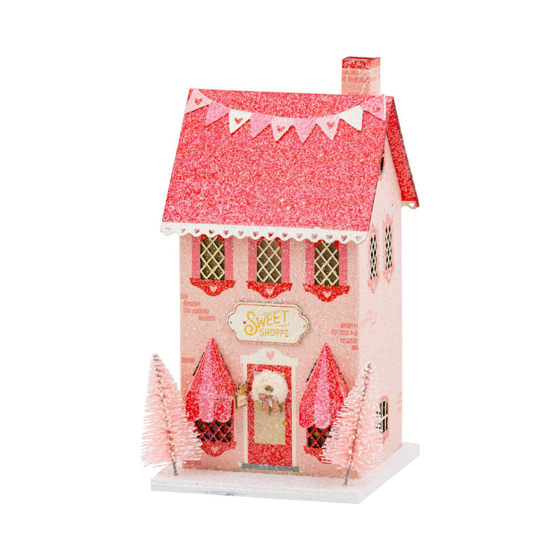 Isolated view of the tall sweet shoppe putz house with pink glitter roof and heart banner valentines decorations.