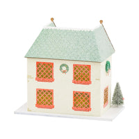 Isolated image of a secondary house design from the Christmas village with a green roof, red shutters, and bottlebrush tree decor.