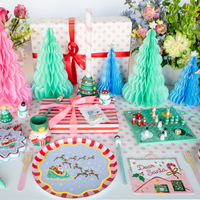 Styled kids' Christmas party table showing the Santa sleigh plates with pastel fabric trees, wrapped gifts, and colorful holiday décor.