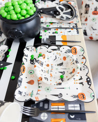  Overhead view of a kids’ place setting with the Halloween bowl nested inside a coordinating scalloped dinner plate on a black-and-white striped runner.