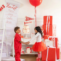 Two children holding hands in front of the decorated Christmas table featuring the party supplies plates and cake.