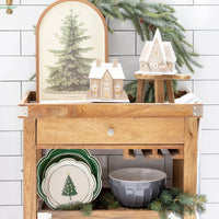 The green scalloped plates layered beneath a small tree plate on a wooden bar cart, functioning as decorative holiday charger plates.