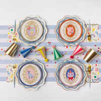 Overhead view of a pastel cat-themed birthday tablescape featuring the round cameo dessert plates layered over scalloped plates, paired with party hats and gold cups.