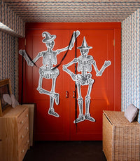 Two dancing skeletons on a red door with wooden dresser in the foreground.