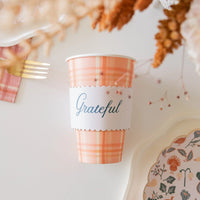 Overhead shot of a single plaid cup with wrap on a white surface and dried florals.