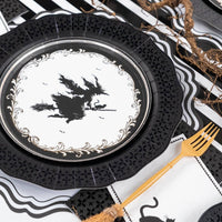 Layered Halloween table setting featuring a black die-cut plate used as a charger beneath a witch silhouette dessert plate and a gold fork.