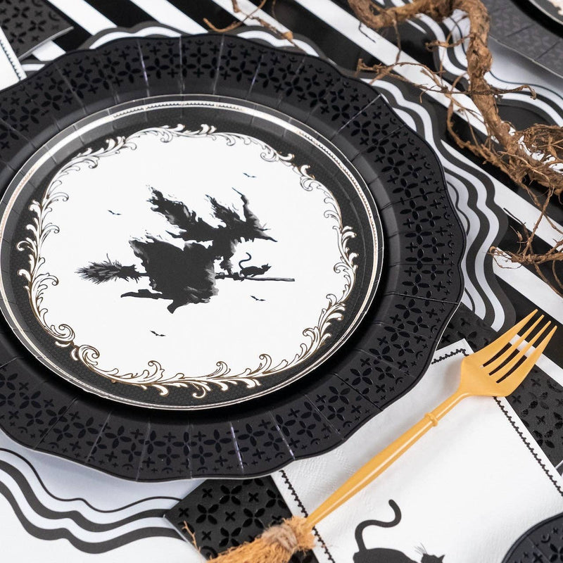 Layered Halloween table setting featuring a black die-cut plate used as a charger beneath a witch silhouette dessert plate and a gold fork.