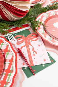Angled close-up of the pink holiday present napkin layered under a solid green napkin and a plaid scalloped napkin.