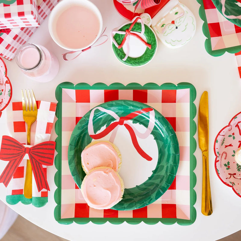 Overhead view of a layered place setting with the wreath shaped plate on a plaid base plate, surrounded by gold cutlery and treats.