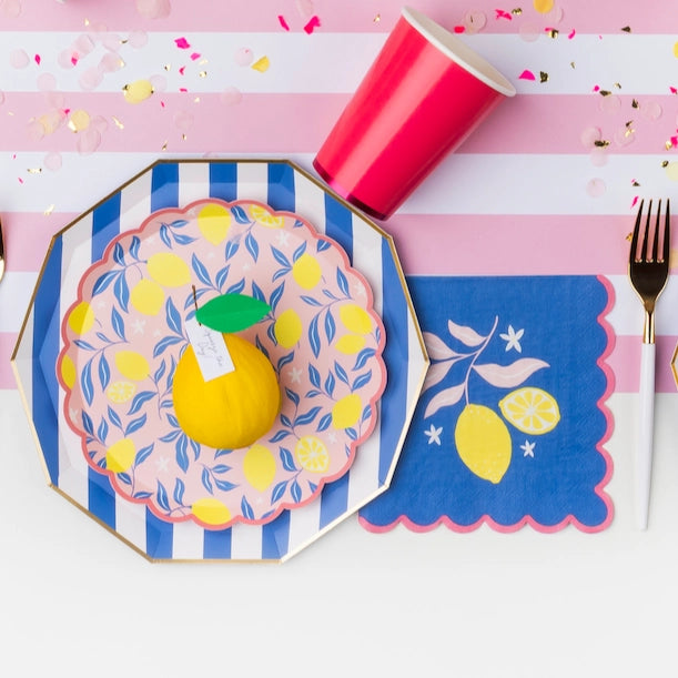 Lemon‑themed place setting with layered blue stripes, citrus plates, cobalt lemon napkin, and gold flatware.