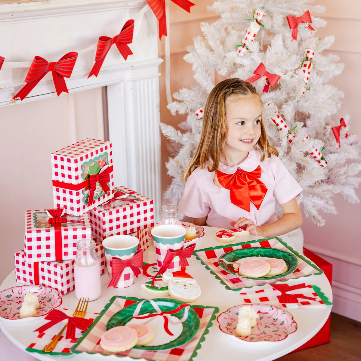 Child at a small table decorated with gingham party supplies crackers, plates, and gift boxes.