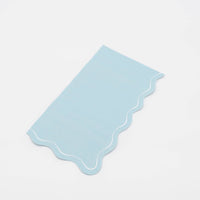 Folded light blue guest towel on a plain surface showing the blue color and wavy scalloped edge.