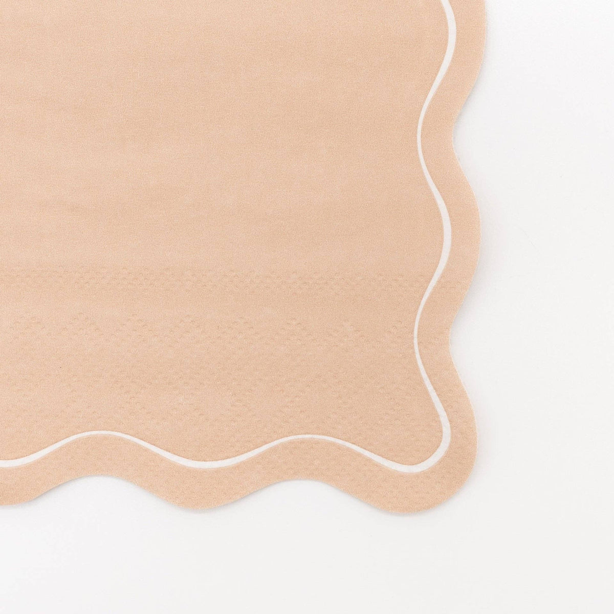 Close-up of a solid light brown paper guest towel in warm tan showing the embossed texture and a flowing wavy scalloped edge outlined in white.