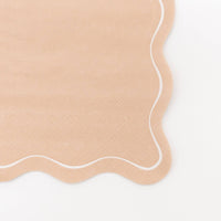 Close-up of a solid light brown paper guest towel in warm tan showing the embossed texture and a flowing wavy scalloped edge outlined in white.