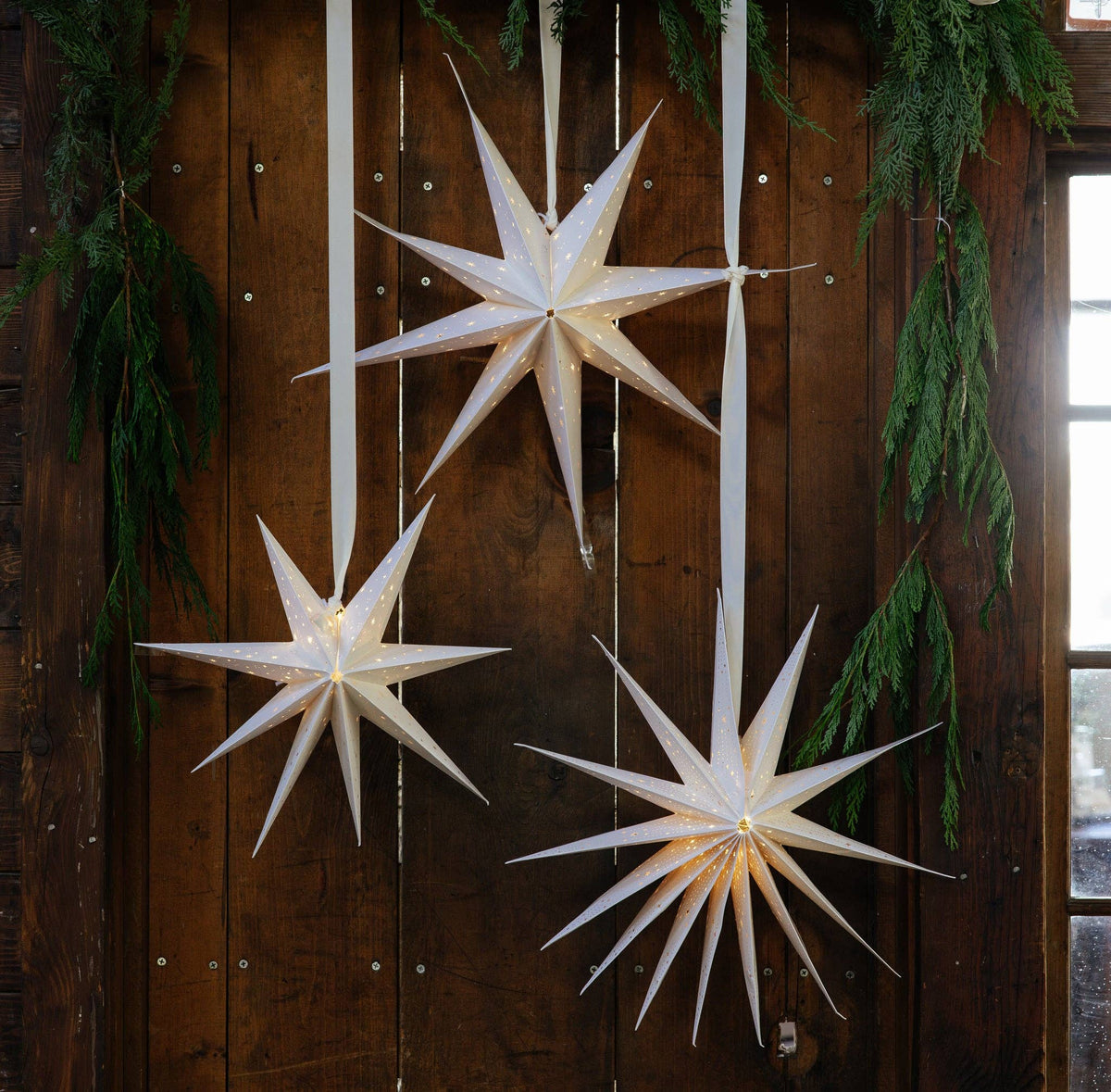 Three lit cream paper stars in graduated sizes hanging together.