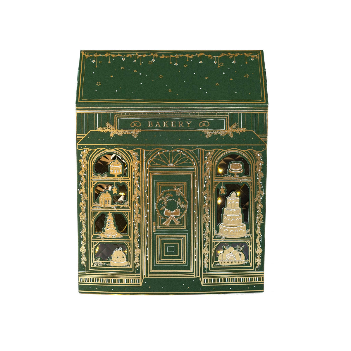 Front view of the green and gold foil paper bakery with tiered cakes and gingerbread in the lit windows