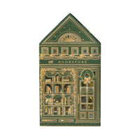 Front view of the tall green and gold foil paper bookstore with a wreath on the door and lit bookshelves