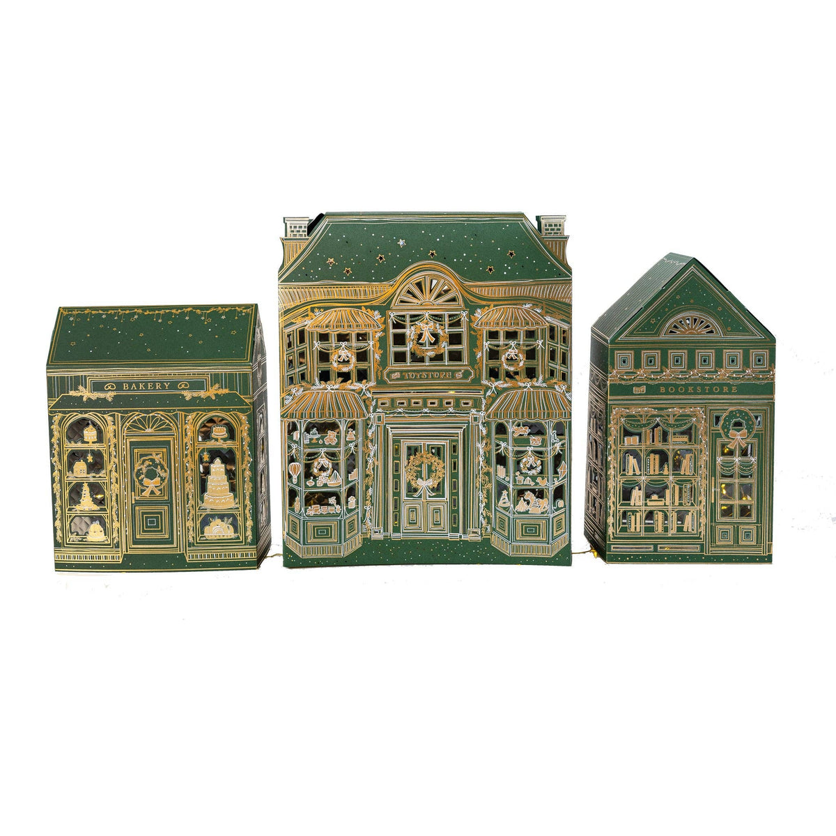 Set of 3 green and gold foil paper Christmas village shops, a bakery, toy store, and bookstore, lined up on white