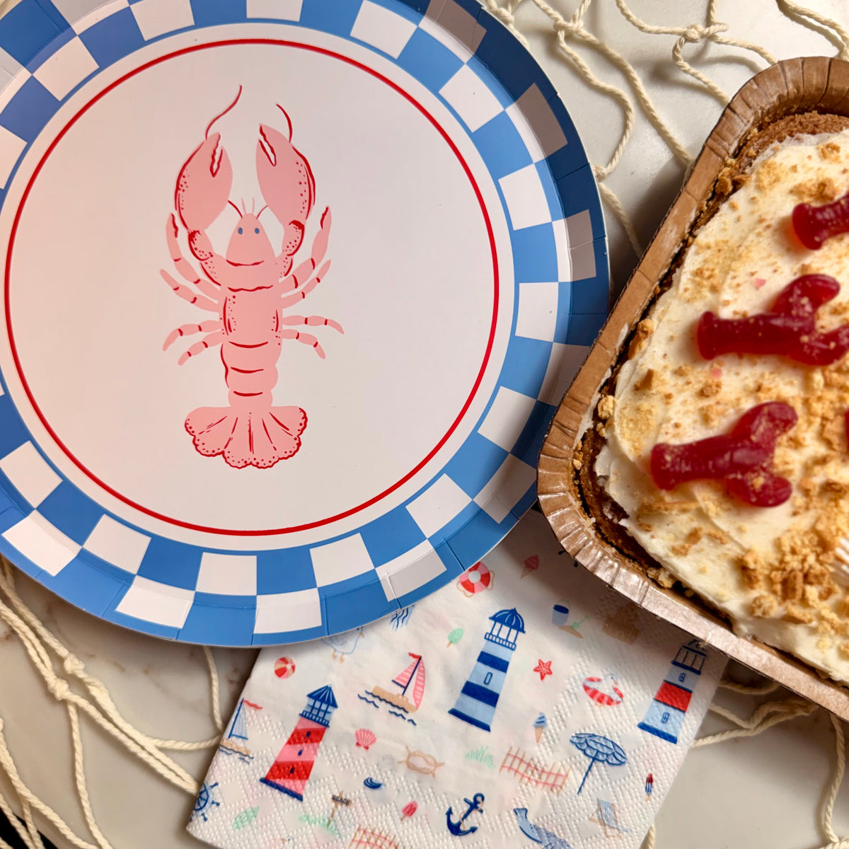 Lobster-themed plate with a checkered border, a dessert in a wooden container, and a nautical-themed napkin.
