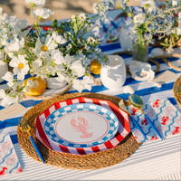 Close-up of lobster paper plate on rattan charger styled at a coastal summer table setting with lobster napkins and white wildflowers