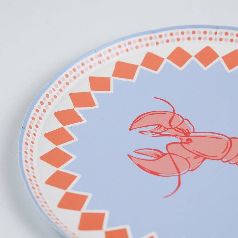 Close-up angled shot of the upper-right quadrant of the lobster paper plate. The orange diamond-check border is in sharp focus — large coral-orange diamond shapes in a single row creating a zigzag silhouette against a white band. An outer ring of pink-mauve dotted dots borders the edge. The periwinkle blue center ground and partial red lobster illustration visible at lower right.