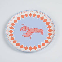 Single lobster print paper salad plate on a white surface, photographed slightly above straight-on. Full plate visible: periwinkle blue center ground with a red-and-pink line-drawn lobster facing left, claws extended. Orange diamond-check border around the full circumference with a pink dotted outer ring. Blue tinted edge visible at plate rim.