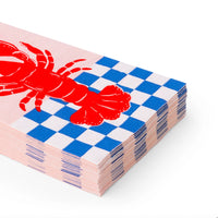 Close‑up angle of stacked lobster guest towels showing red lobster graphic and blue picnic checkerboard border.