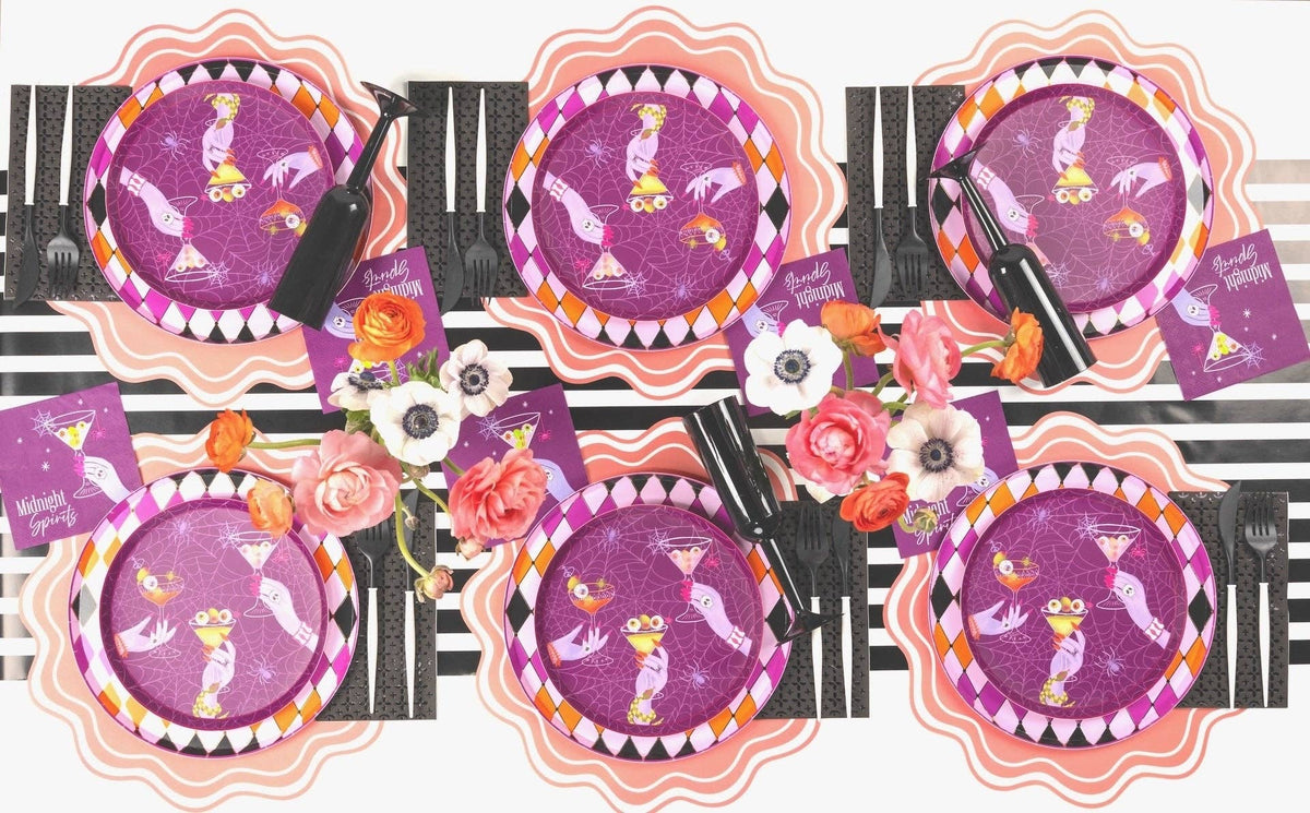 Wide overhead shot of a long dining table set with eight purple cocktail party paper plates and black tableware.