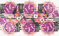 Wide overhead shot of a long dining table set with eight purple cocktail party paper plates and black tableware.