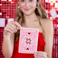Woman holding lucky card napkin in front of red party backdrop