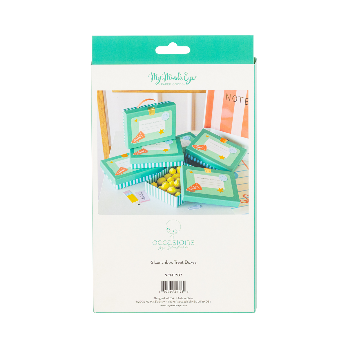 Back of lunchbox shaped treat box packaging showing styled product scene with teal boxes stacked and filled with yellow candies on white desk