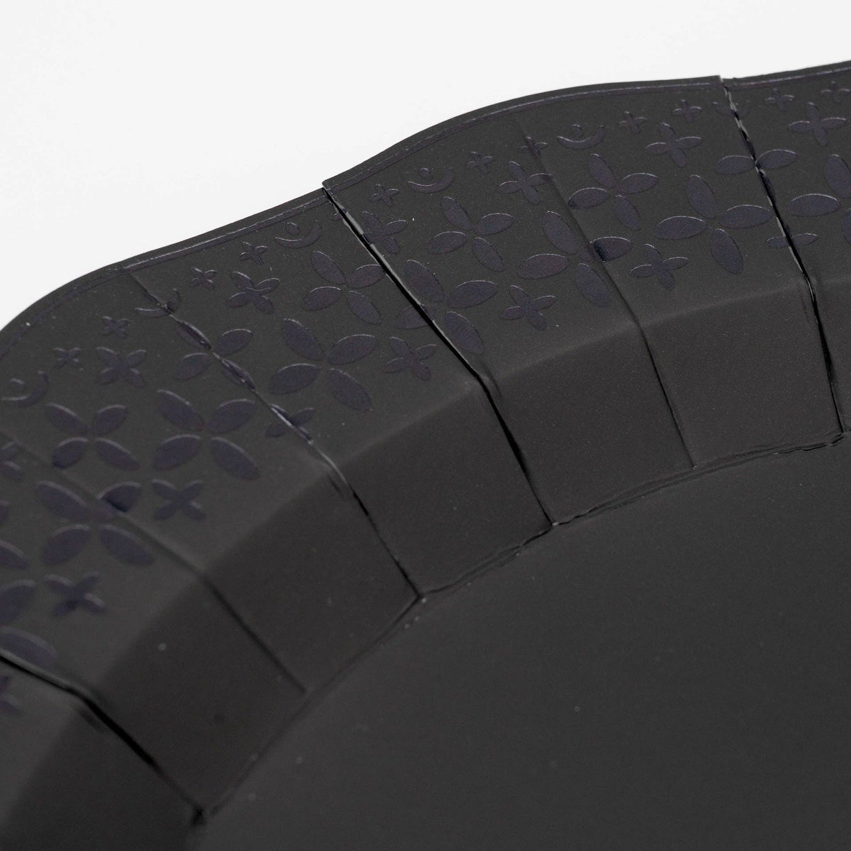 Extreme macro detail highlighting the precision laser-cut cross and floral patterns on the black paper plate border.