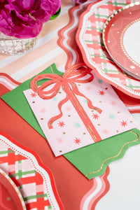 Close-up macro detail of three layered holiday paper napkins showing a pink gift design, solid green, and scalloped red plaid.