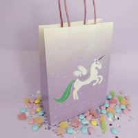 Side view of a unicorn gift bag surrounded by pastel candies and glitter