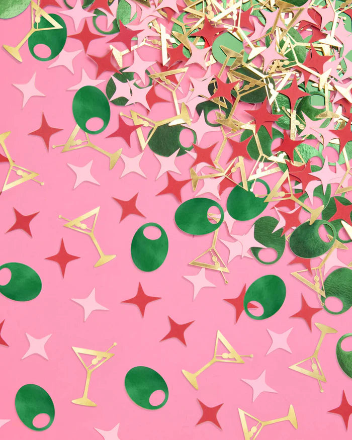Pile of martini party foil confetti in gold, green, pink, and red shapes scattered across pink background