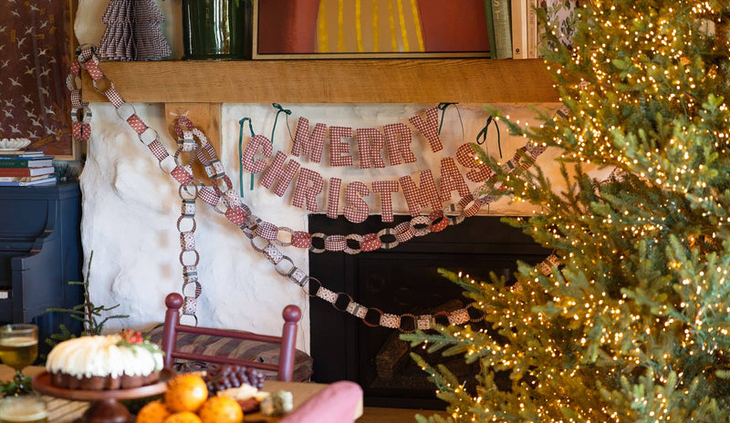 Puffy fabric merry christmas banner on white fireplace with paper chain garland and lit tree