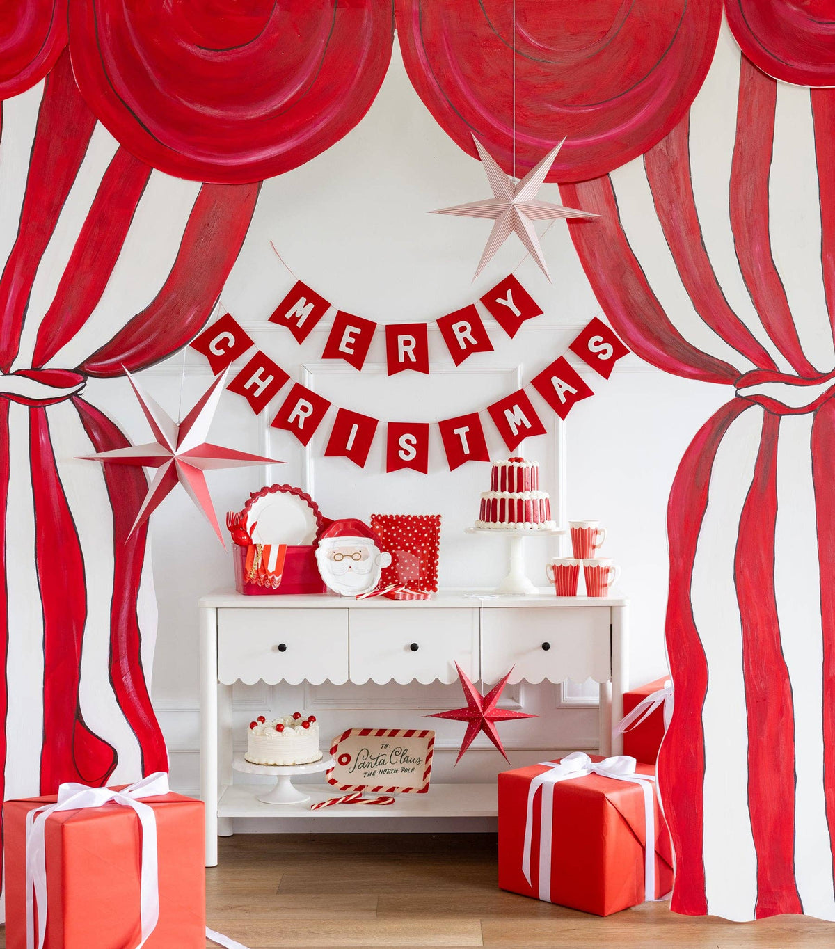 The Merry Christmas felt banner strung on a mantel against a red-and-white striped backdrop with red balloons.