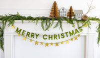 Merry Christmas flocked banner hung on a door with garland and mini trees
