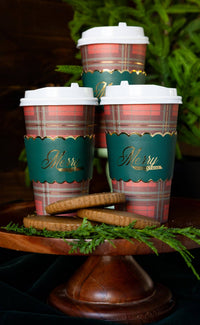 Three Merry Christmas plaid to go cups styled with greenery