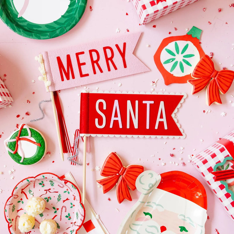 Close-up of ‘Merry’ and ‘Santa’ felt pennants surrounded by plates, cookies, and gifts.